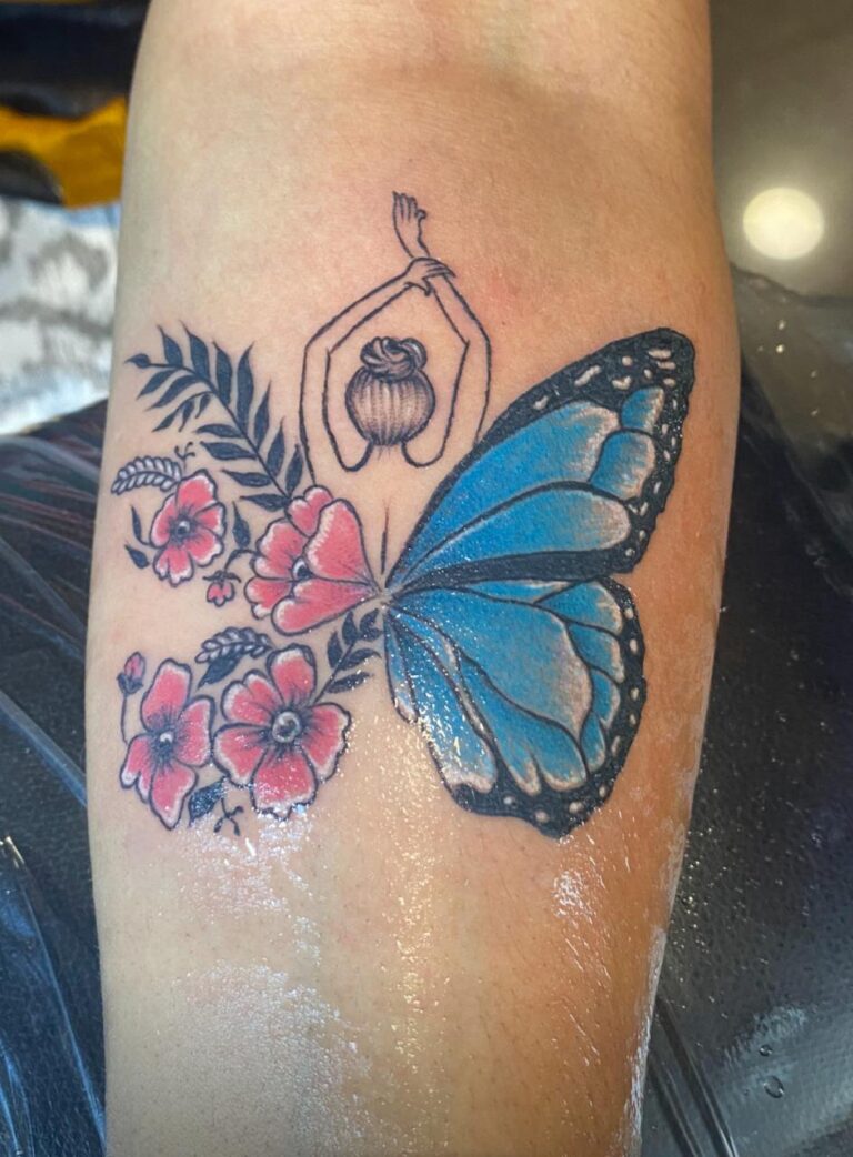 The image shows a tattoo featuring a woman with her arms raised above her head. Her body transitions into a vibrant blue butterfly wind on one side, and on the other side it's with delicate pink flowers and green leaves.