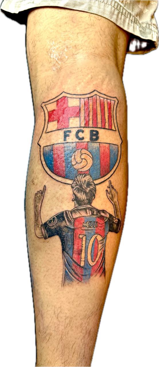 A detailed colourful portrait tattoo featuring Lionel Messi wearing his number 10 jersey, raising his hands toward the large FC Barcelona club crest above him.