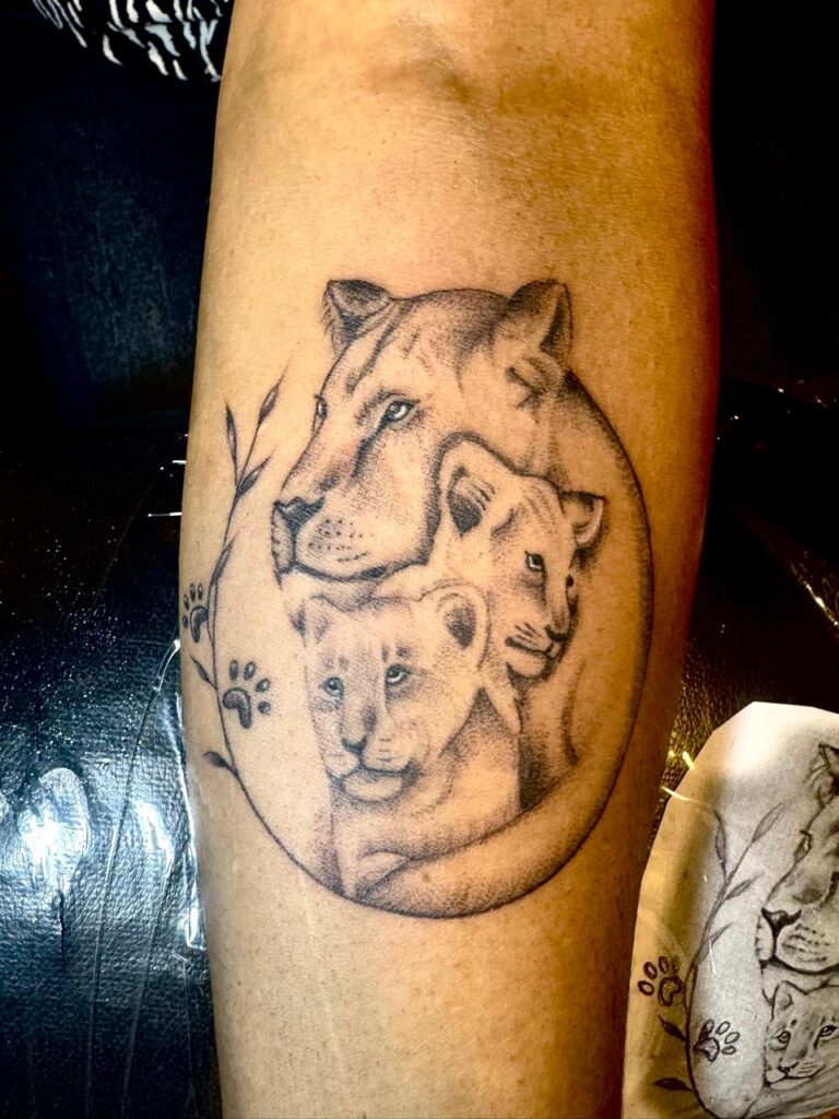 The image shows a lioness embracing two cubs black and grey tattoo.