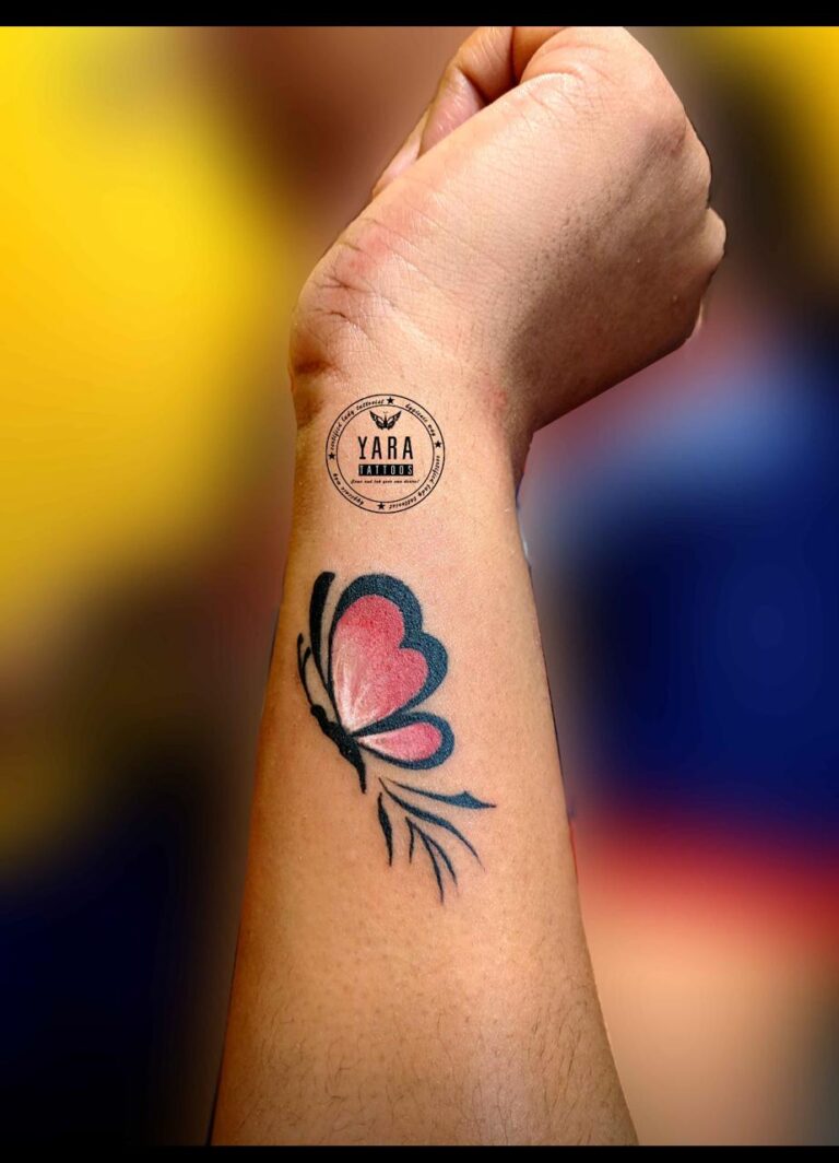 The image shows a beautiful butterfly minimal tattoo on the wrist featuring pink and black ink.