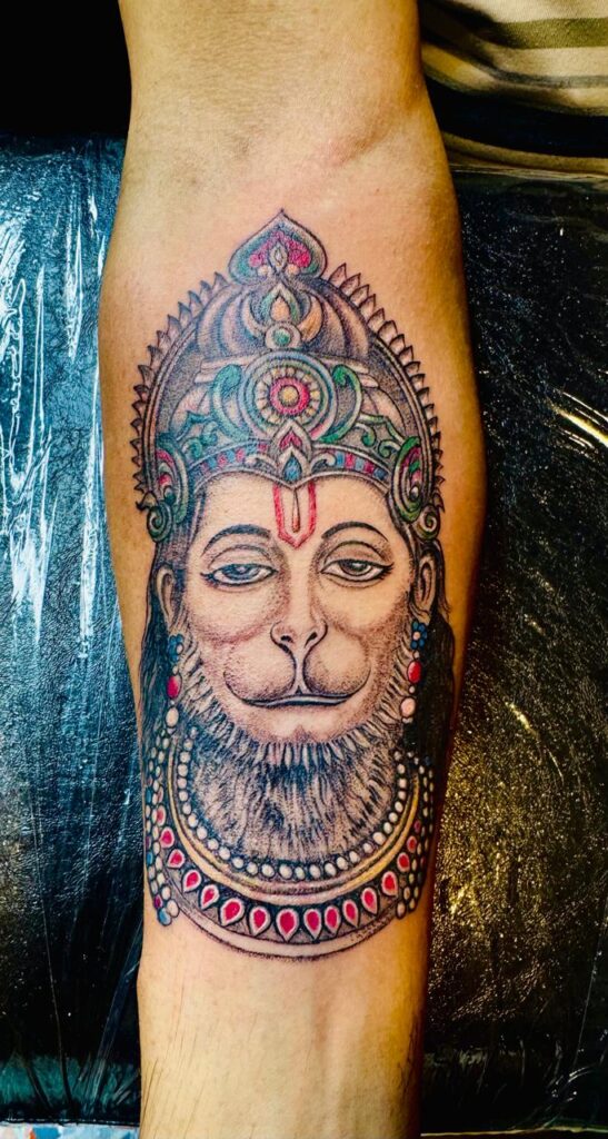 The image shows a permanent tattoo depicting the colorful face of Lord Hanuman on the forearm.