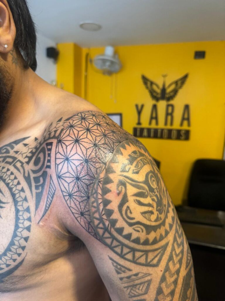The image shows an intricate geometric, tribal tattoo on a man’s shoulder and upper arm.