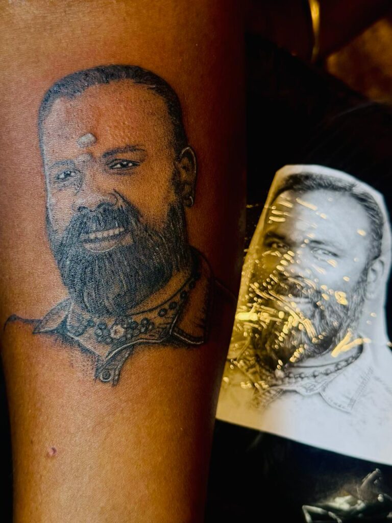The image shows a realistic human portrait tattoo in black on a person’s arm.