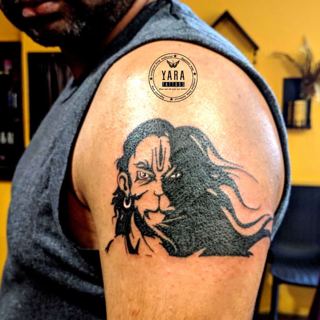 Shoulder tattoo featuring bold black ink portrait of a warrior with flowing hair, detailed linework and strong artistic shading on upper arm.