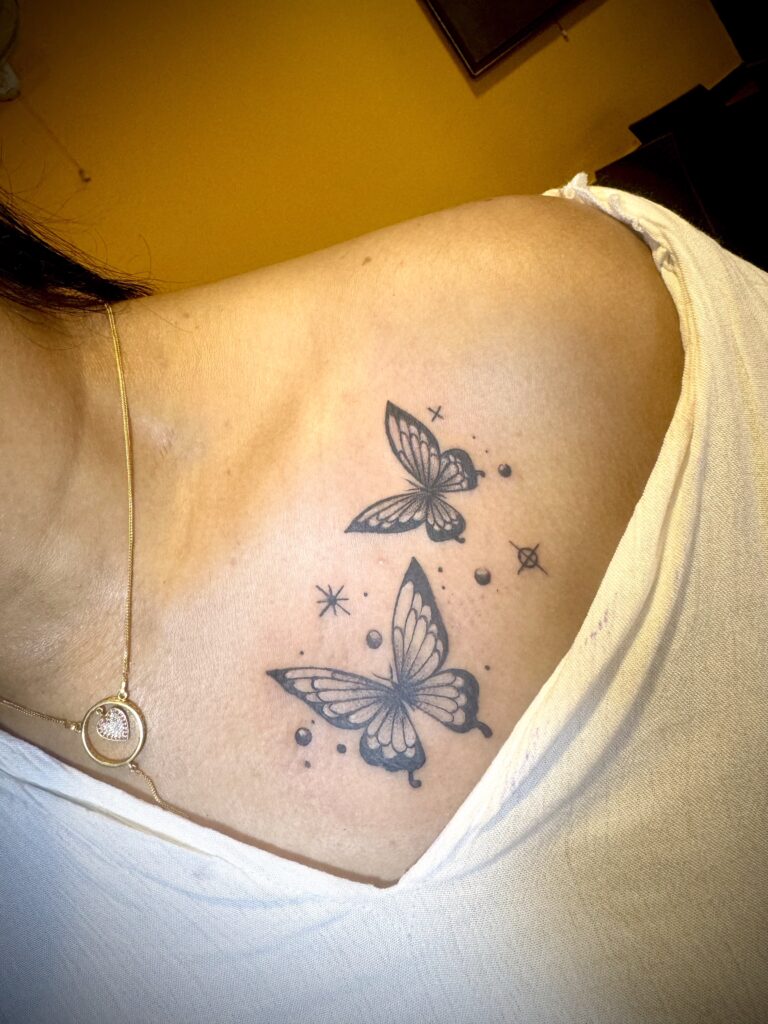 Blackwork butterfly tattoo on shoulder showing bold dark ink butterflies with clean lines simple shading modern tattoo style design artwork