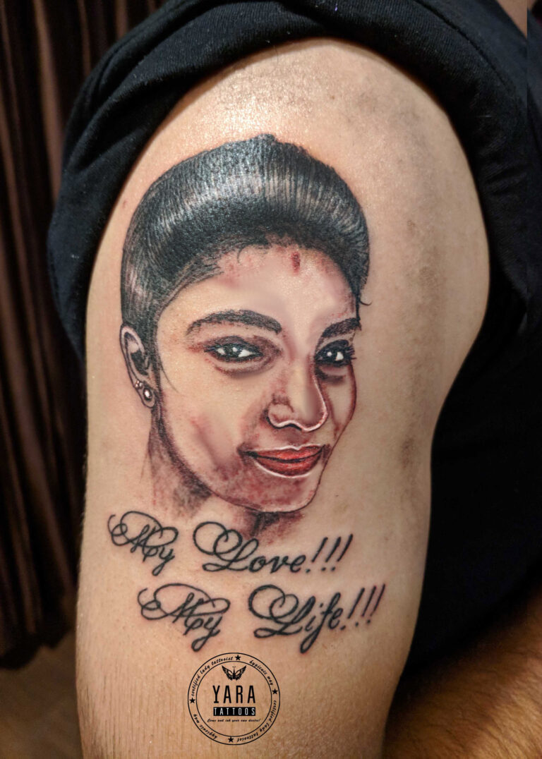 Realistic color portrait tattoo of a woman’s face inked on the upper arm, featuring soft shading, expressive eyes, and the words “My Love!!! My Life!!!” written below in cursive script.