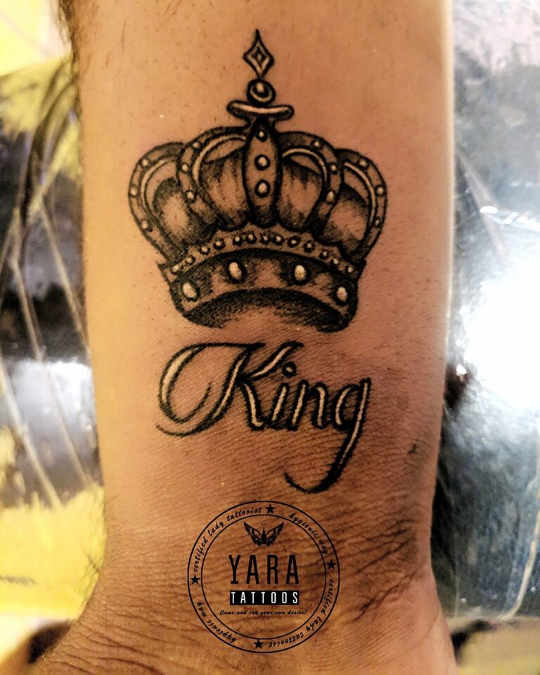 Black crown tattoo with word King written below it on wrist.