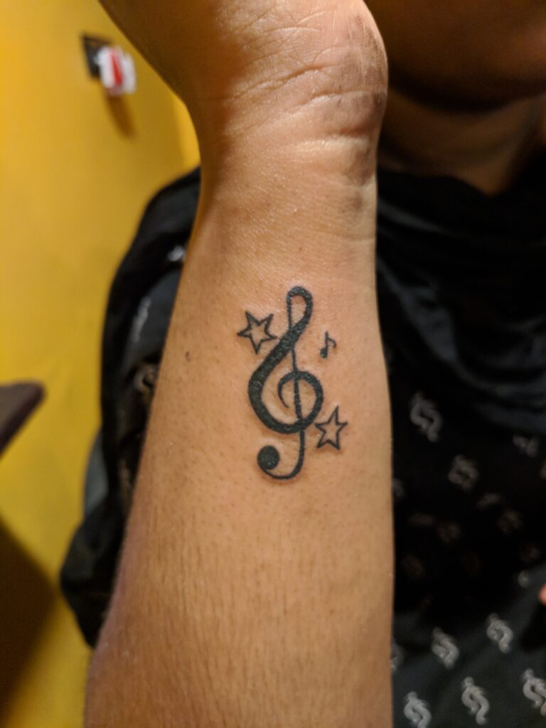 Small music note tattoo on wrist showing slight fading edges where touch up helps restore dark ink clarity over time