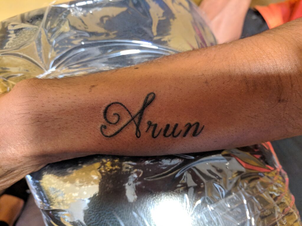 Wrist tattoo featuring cursive lettering of a name in black ink on forearm highlighting clean script style.