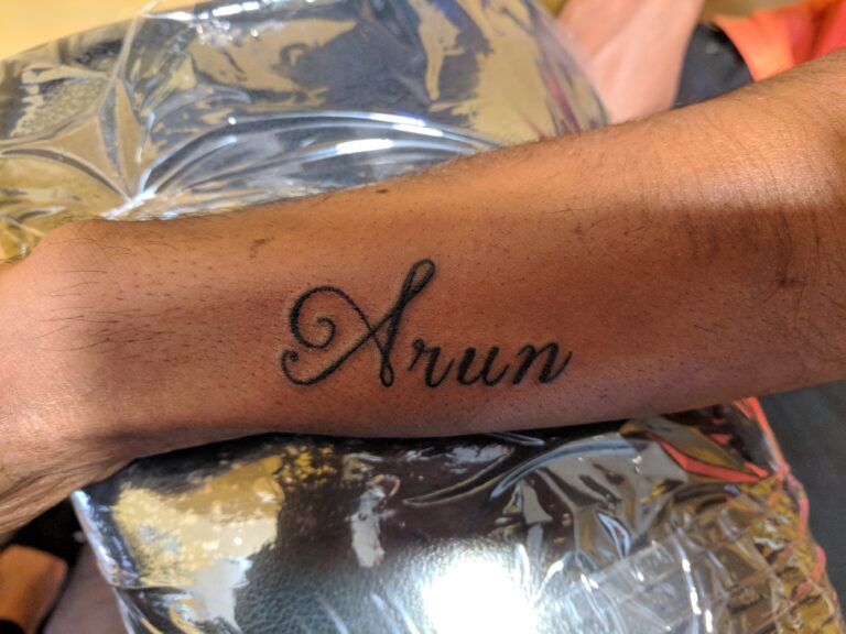 Wrist tattoo featuring cursive lettering of a name in black ink on forearm highlighting clean script style.